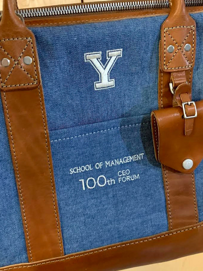 Blue bag with brown handles and trim, featuring a logo and text on a wooden surface.