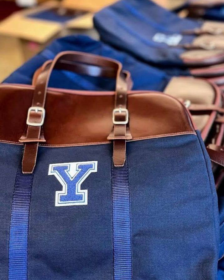 Blue bag with a brown handle and 'Y' logo on a wooden surface