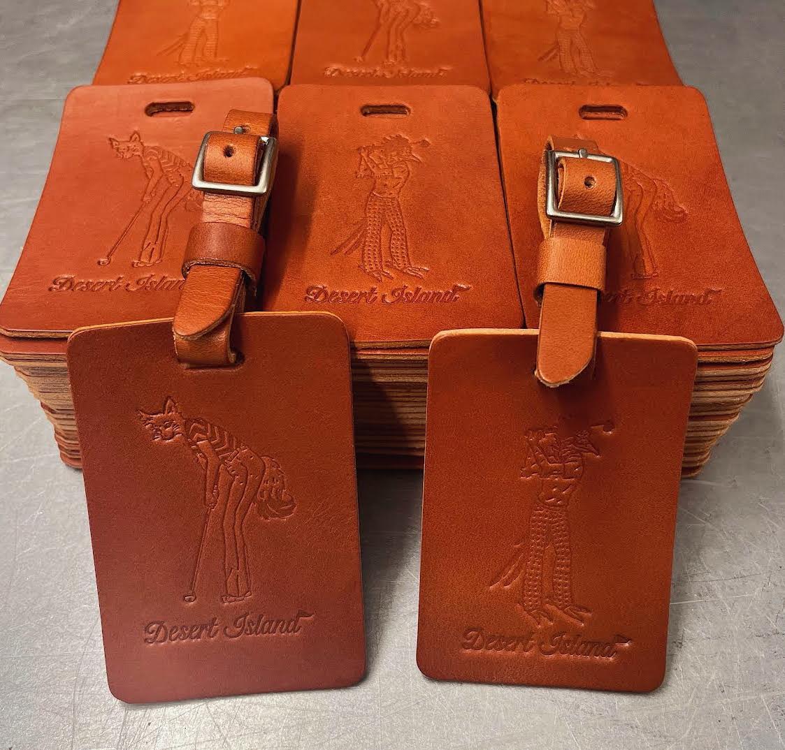 Set of brown leather luggage tags with 'Desert Island' branding on a light gray background