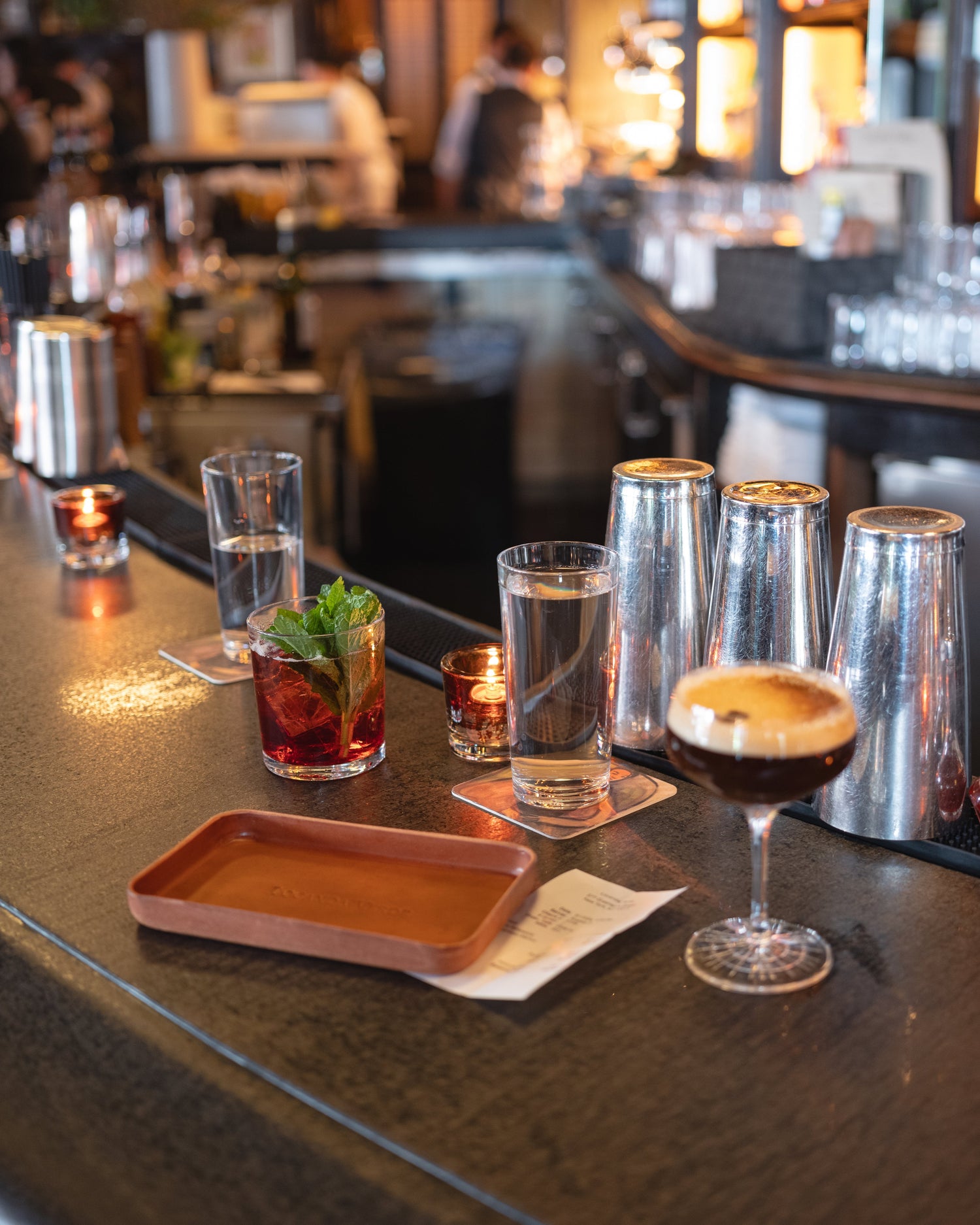 Bar counter with various drinks and bar tools in a dimly lit bar setting