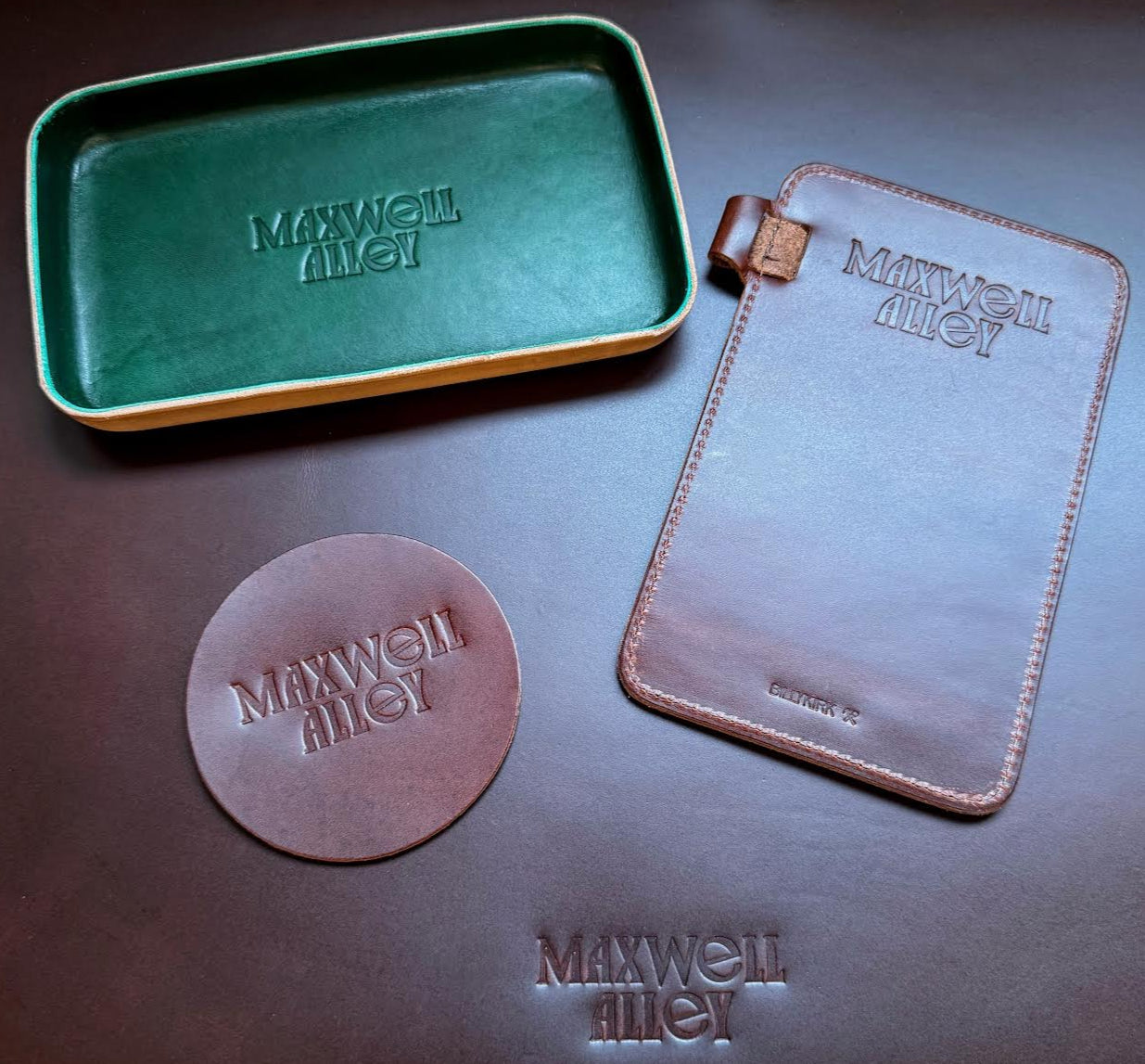Collection of Maxwell & Williams branded leather products on a dark surface