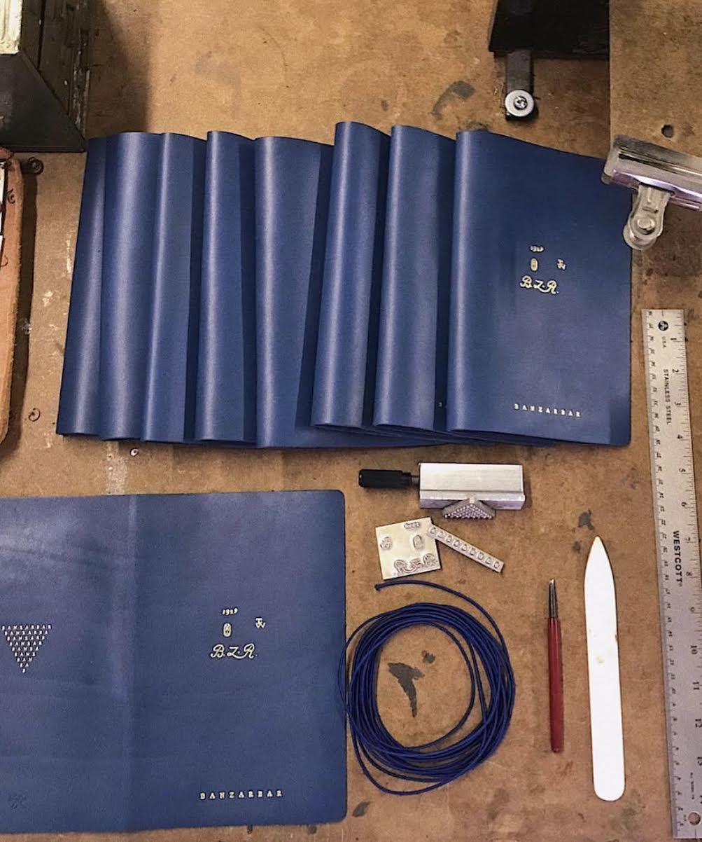 Blue leather-bound books on a wooden surface with tools and a ruler.