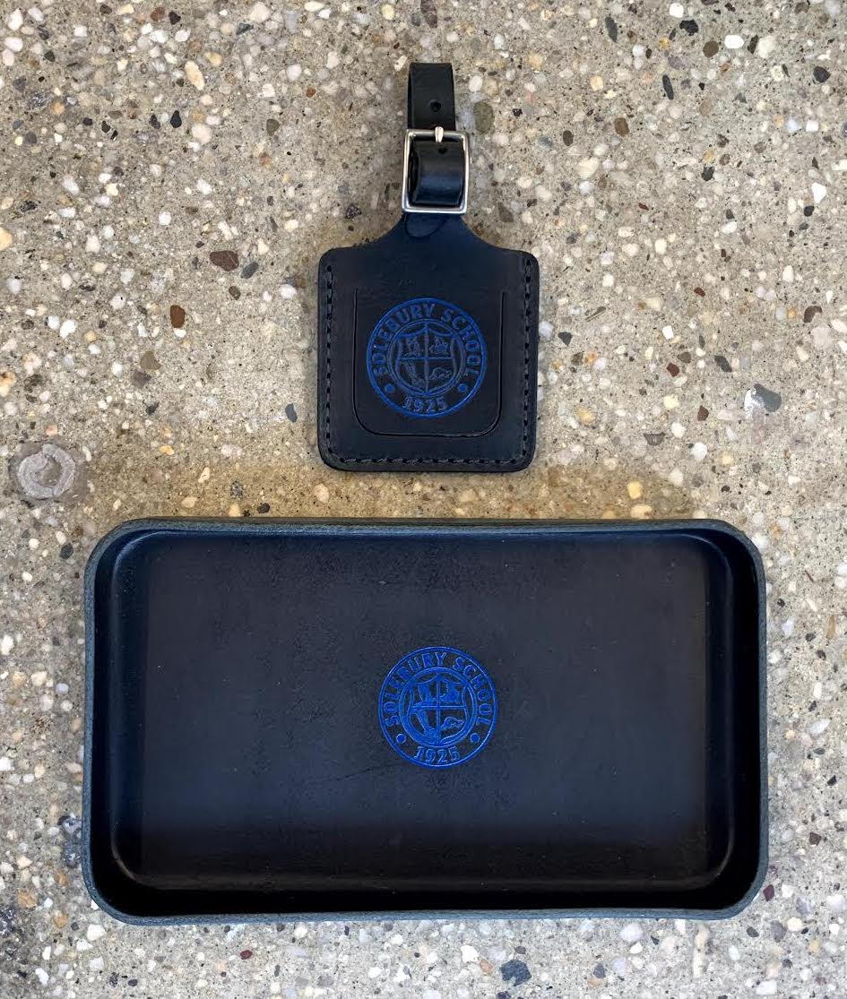 Black leather luggage tag and tray with blue logo on a concrete surface