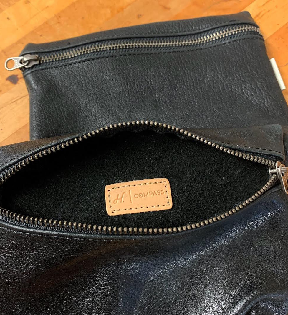Black leather clutch bag with a visible brand label on a wooden surface