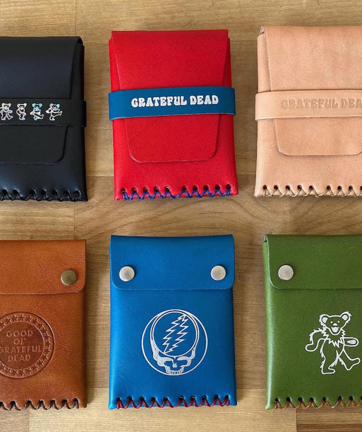 Collection of six leather pouches in various colors on a wooden surface, featuring 'Grateful Dead' branding.