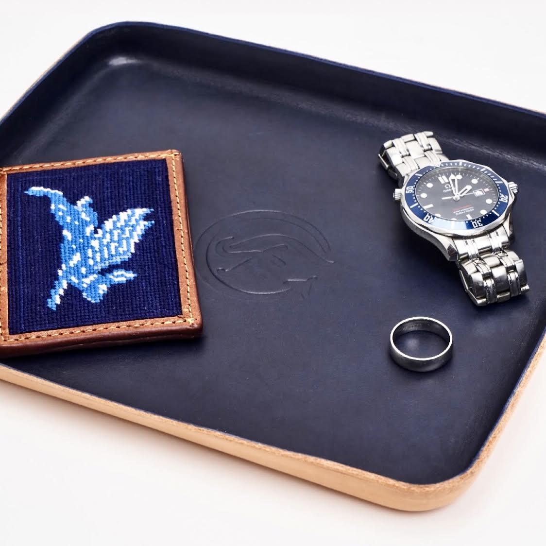 Watch, ring, and embroidered patch on a dark tray with a visible brand logo.