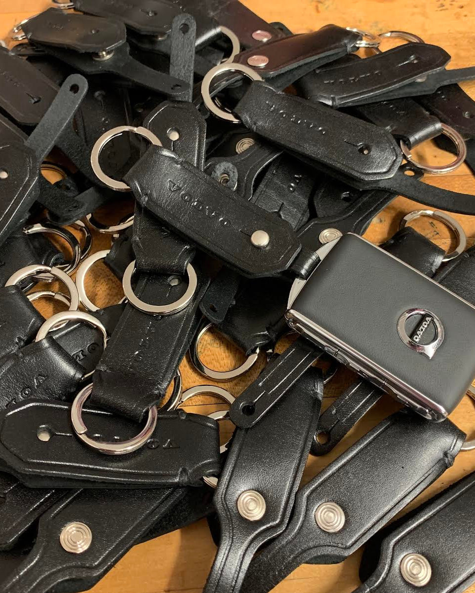 Pile of black leather keychains with metal rings on a wooden surface
