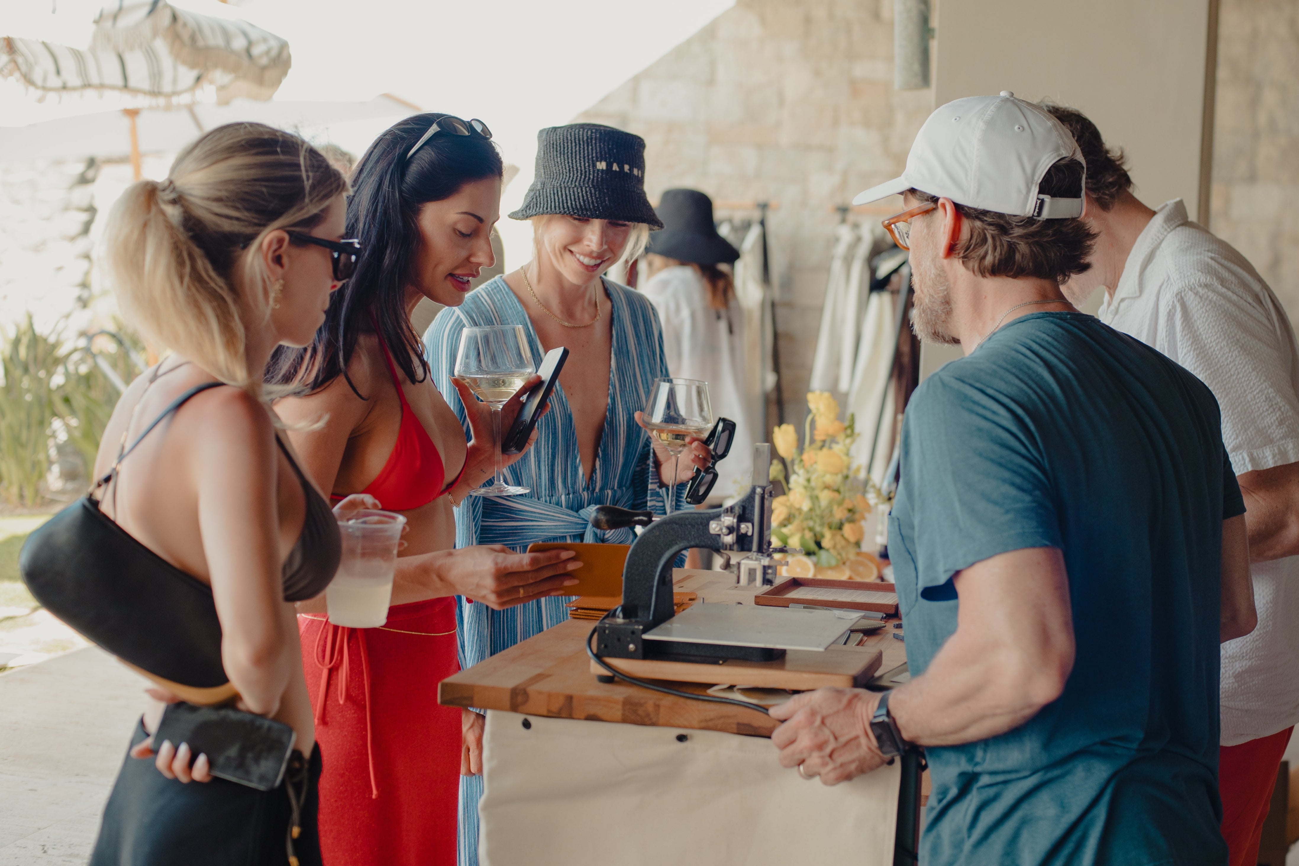 Group of people socializing outdoors near a wooden table with drinks.