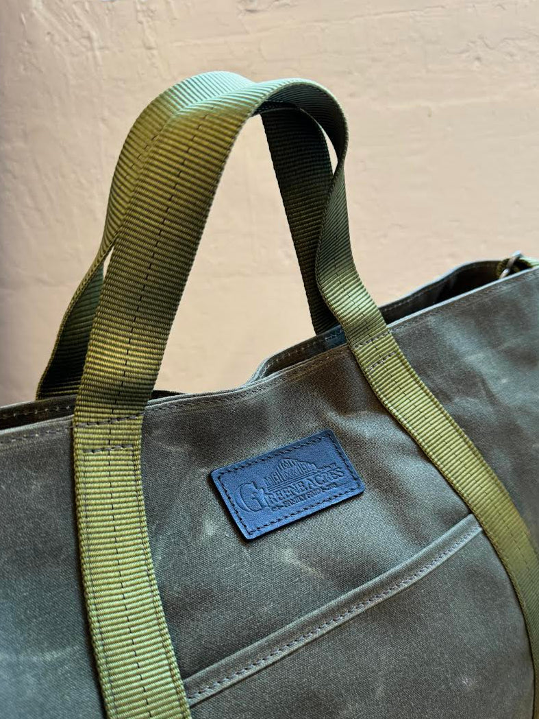 Gray tote bag with green strap and blue label on a beige background