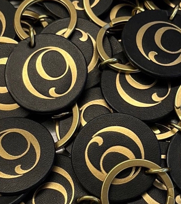 Black and gold circular keychains with a design on a gray surface