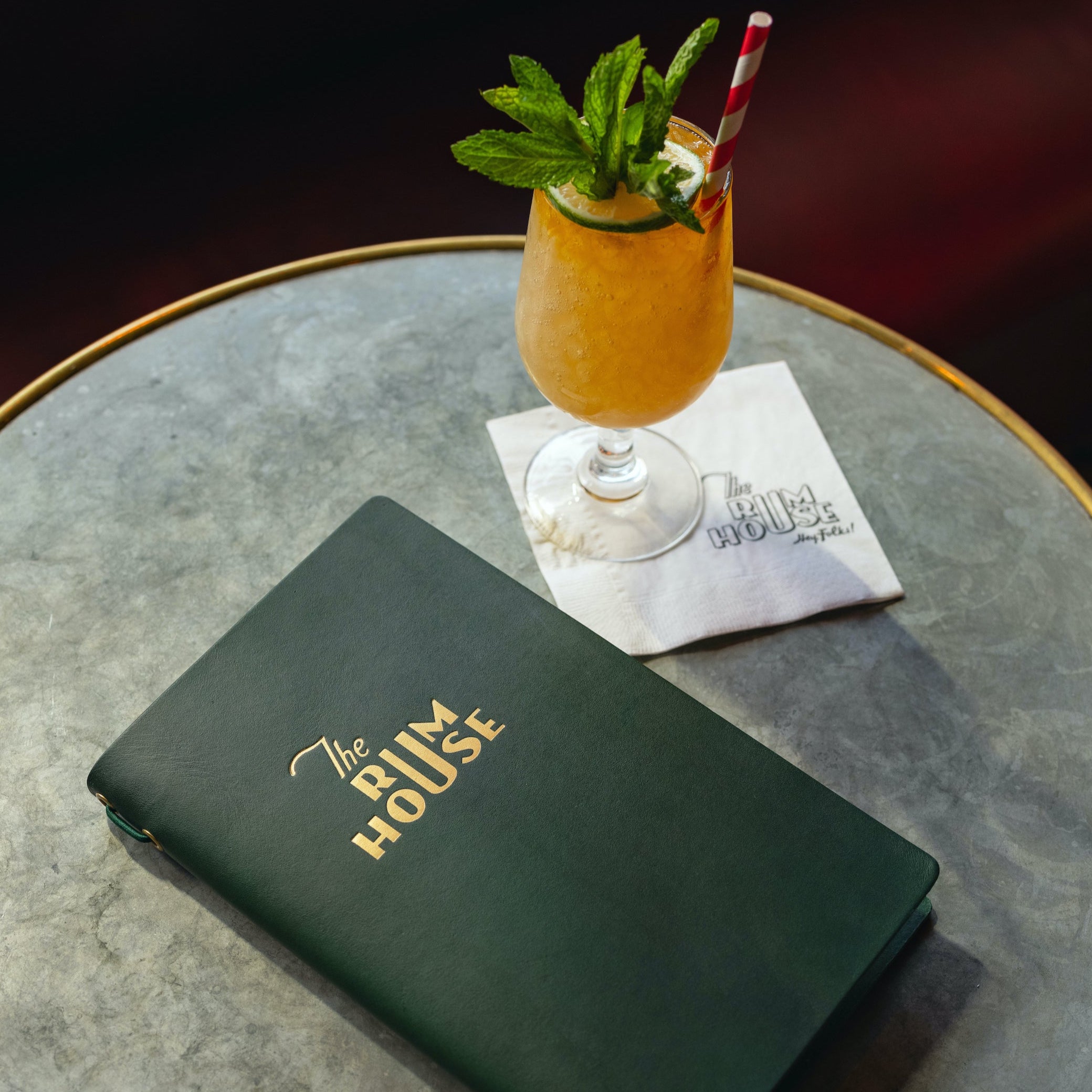 Green menu on a round table with a cocktail garnished with mint leaves and straws.