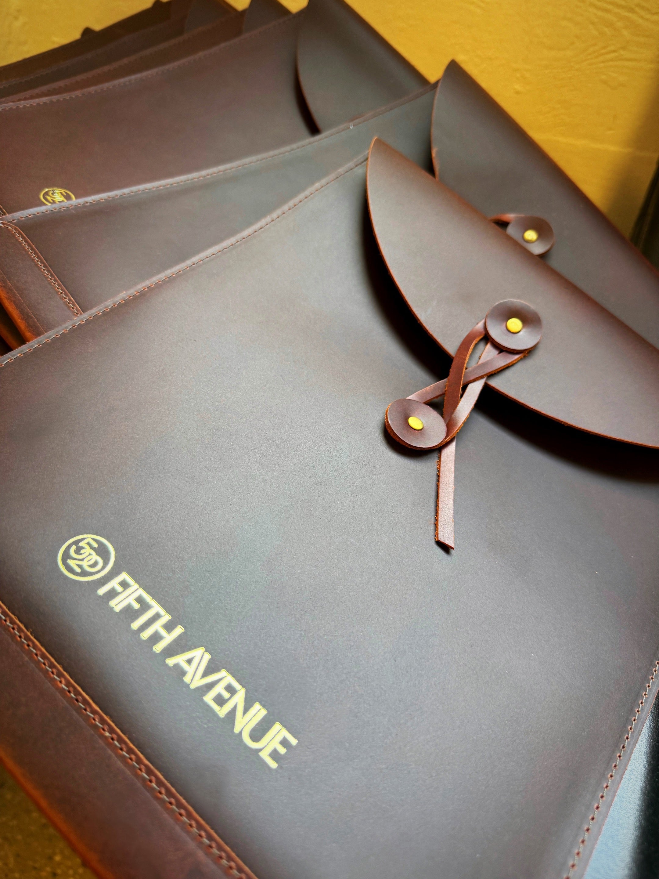 Brown leather bags with 'Fifth Avenue' branding on a yellow background