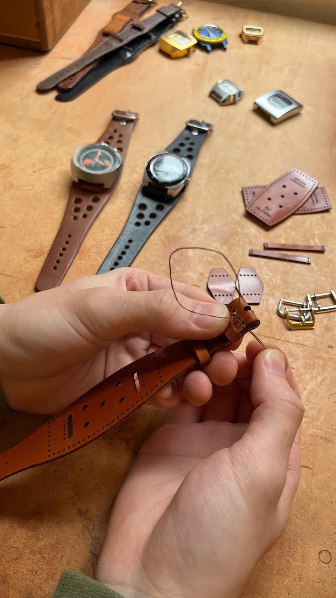 Person working with leather straps and watch parts on a wooden surface