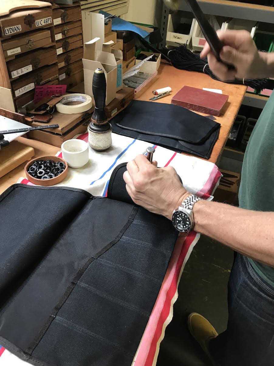 Person working on leather goods with tools and materials on a workbench.